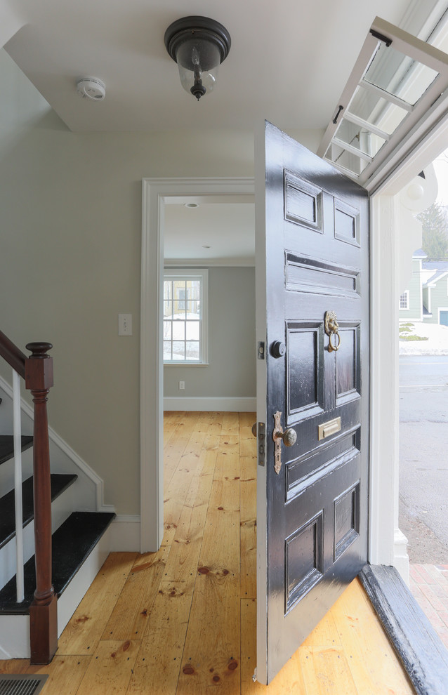 Aménagement d'une petite porte d'entrée classique avec un mur beige, parquet clair et une porte noire.