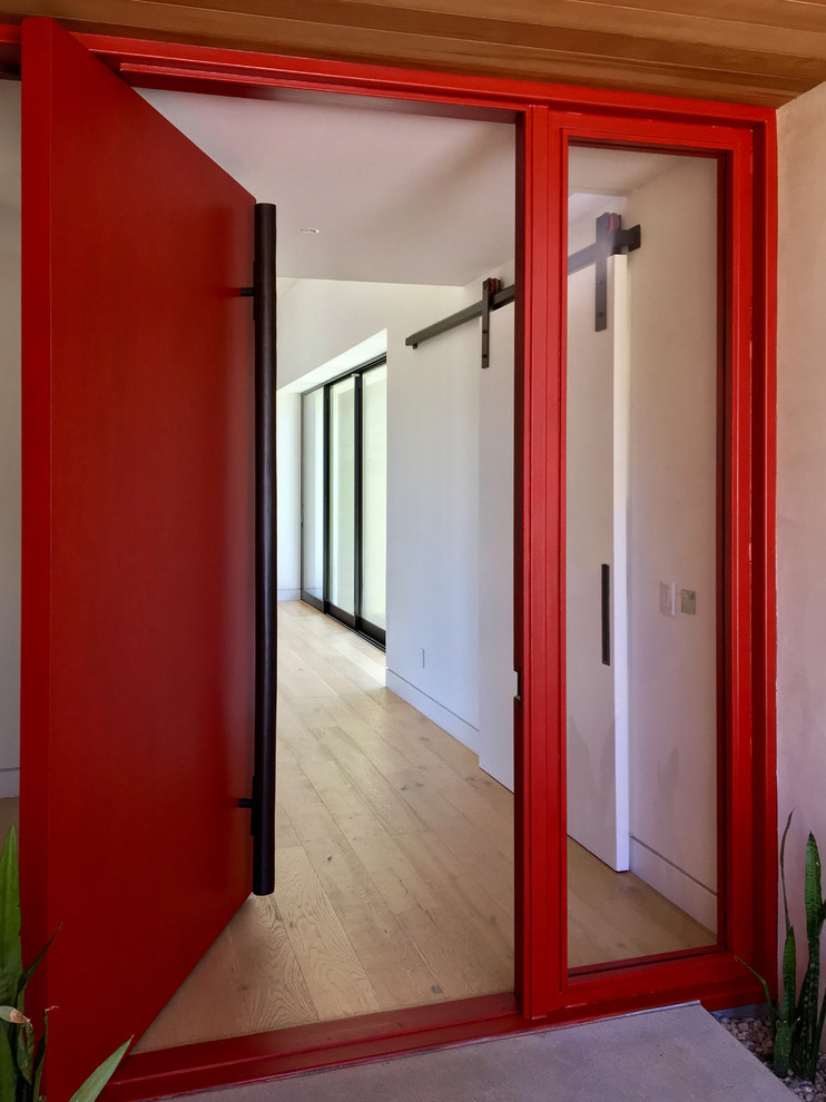 Réalisation d'une grande porte d'entrée minimaliste avec un mur blanc, parquet clair, une porte pivot, une porte rouge et un sol beige.