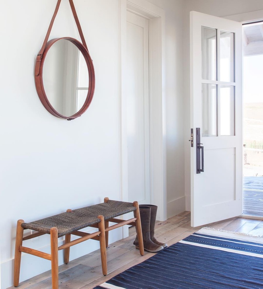 Cette image montre une entrée chalet avec un couloir, un mur blanc, un sol en bois brun, une porte simple, une porte blanche et un sol marron.