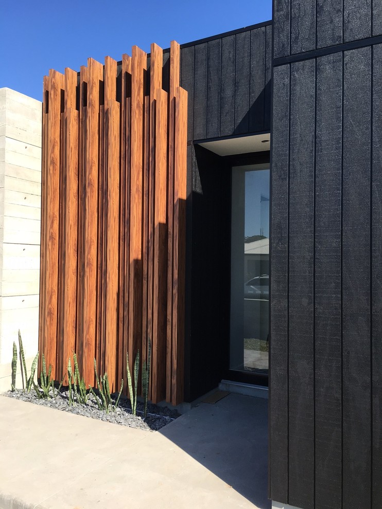 Idée de décoration pour une porte d'entrée design de taille moyenne avec un mur noir, sol en béton ciré, une porte pivot, une porte en verre et un sol gris.