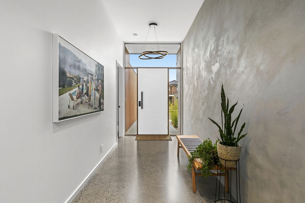 Cette image montre une grande entrée design avec sol en béton ciré, une porte simple, un couloir, une porte blanche, un sol gris et un mur blanc.