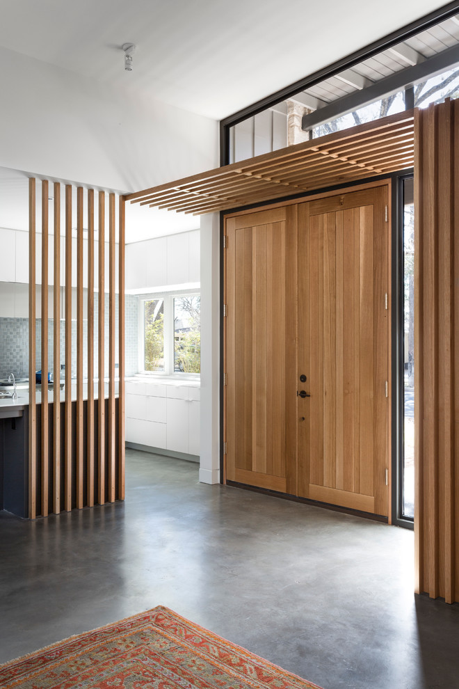 Immagine di un ingresso minimalista con pareti bianche, pavimento in cemento, una porta a due ante e una porta in legno bruno