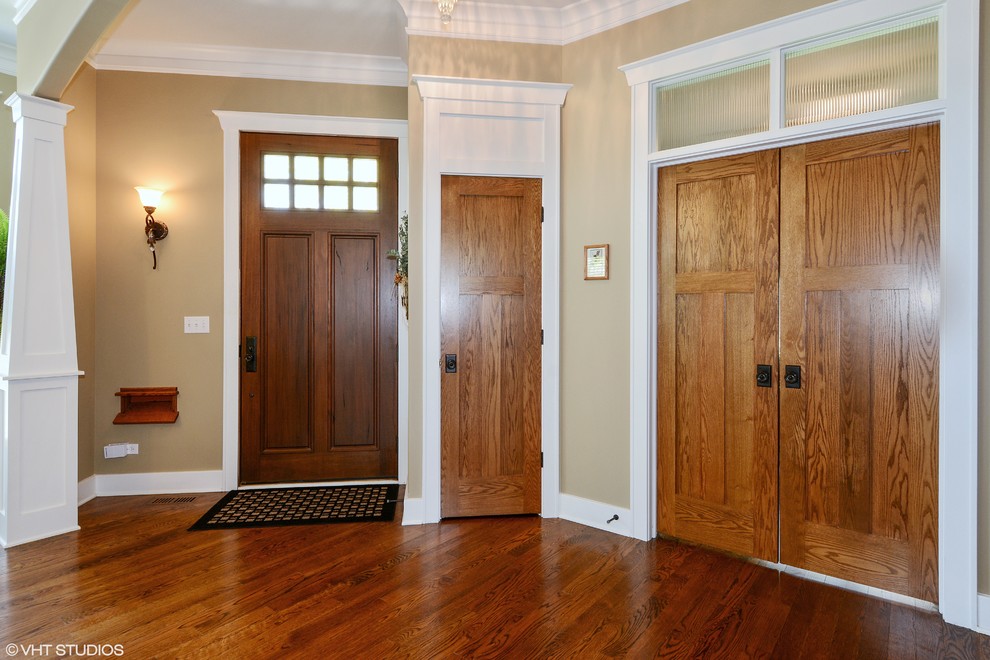Cette image montre un grand hall d'entrée craftsman avec un mur beige, parquet foncé, une porte simple et une porte en bois foncé.