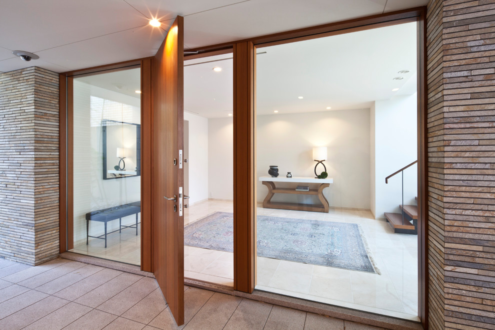 Réalisation d'un grand vestibule minimaliste avec un mur blanc, un sol en marbre, une porte simple, une porte en bois brun et un sol beige.