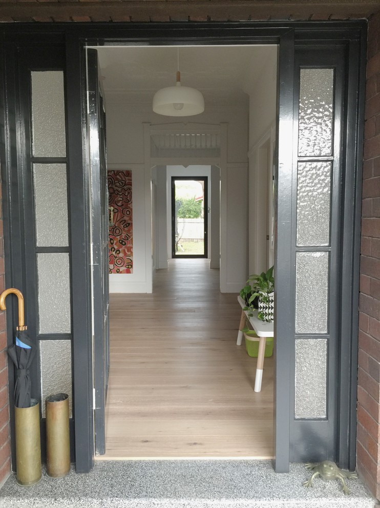 Minimalistisk inredning av en mycket stor foajé, med vita väggar, ljust trägolv, en enkeldörr och en grå dörr