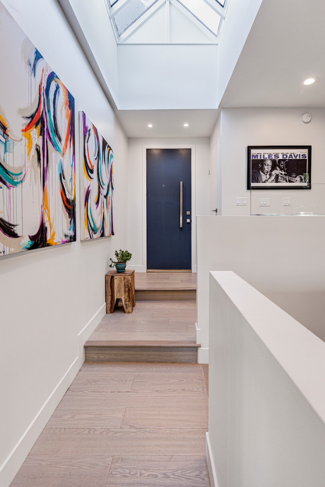 Imagen de hall contemporáneo de tamaño medio con paredes blancas, suelo de madera clara, puerta simple, puerta azul y suelo beige