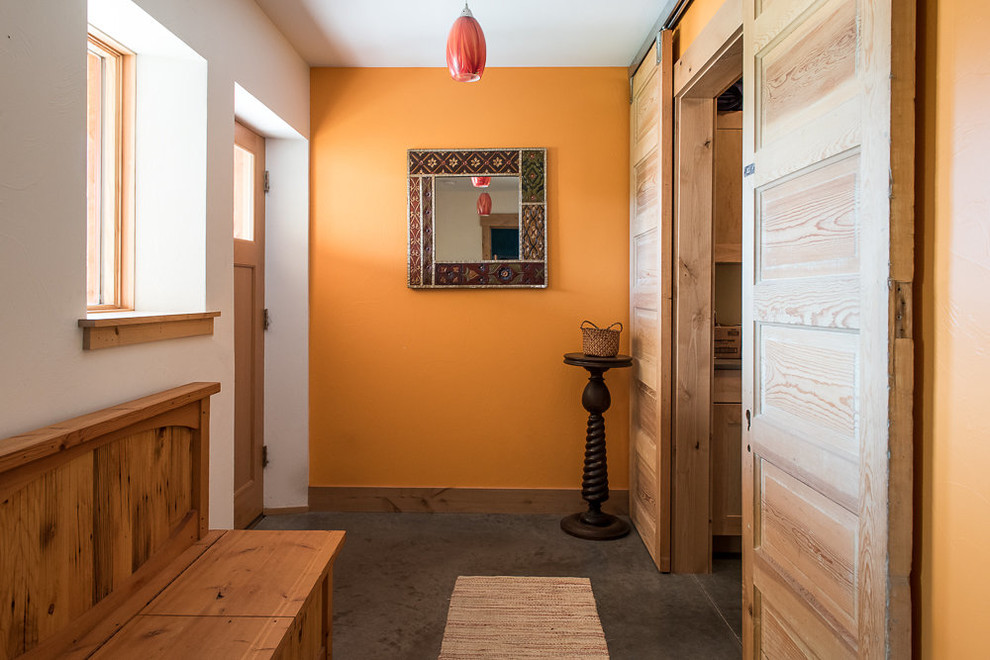 Idée de décoration pour une petite porte d'entrée chalet avec un mur orange, sol en béton ciré, une porte simple, une porte en bois brun et un sol gris.