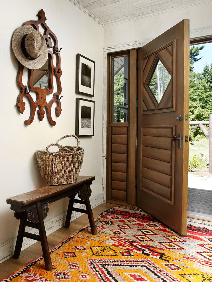 Cette image montre une entrée chalet avec un mur blanc, un sol en bois brun, une porte simple et une porte en bois brun.