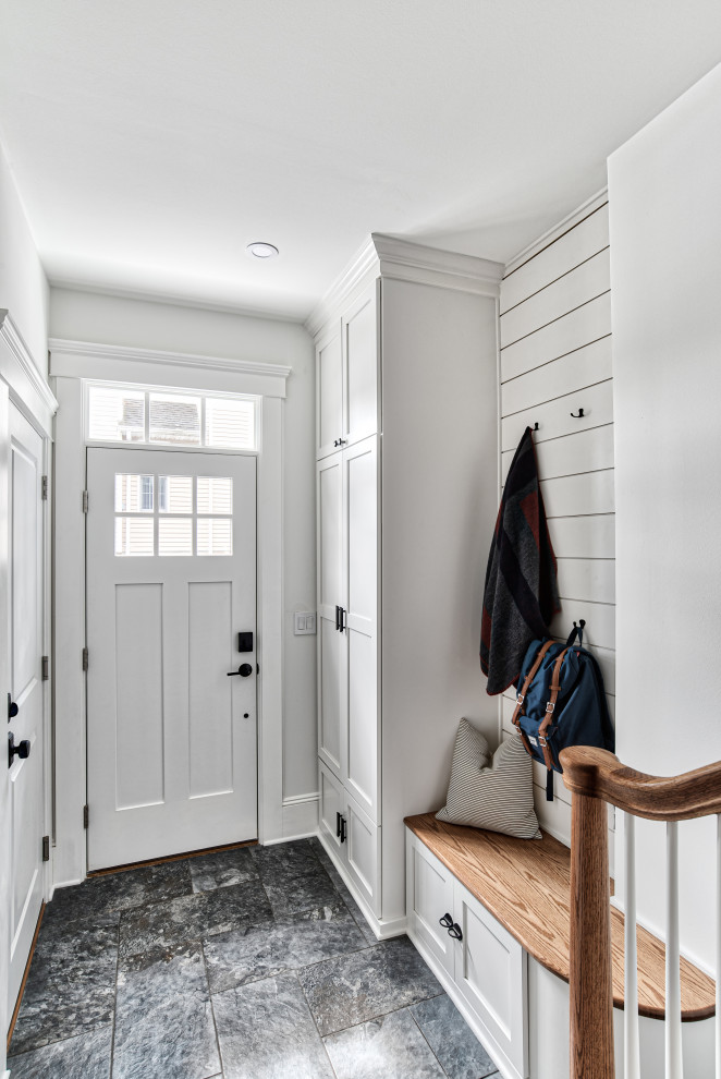 Klassisk inredning av ett kapprum, med vita väggar, en enkeldörr, en vit dörr och grått golv