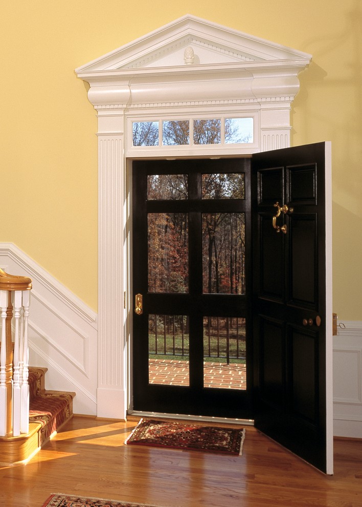 Imagen de distribuidor clásico grande con paredes amarillas, suelo de madera en tonos medios, puerta simple y puerta negra