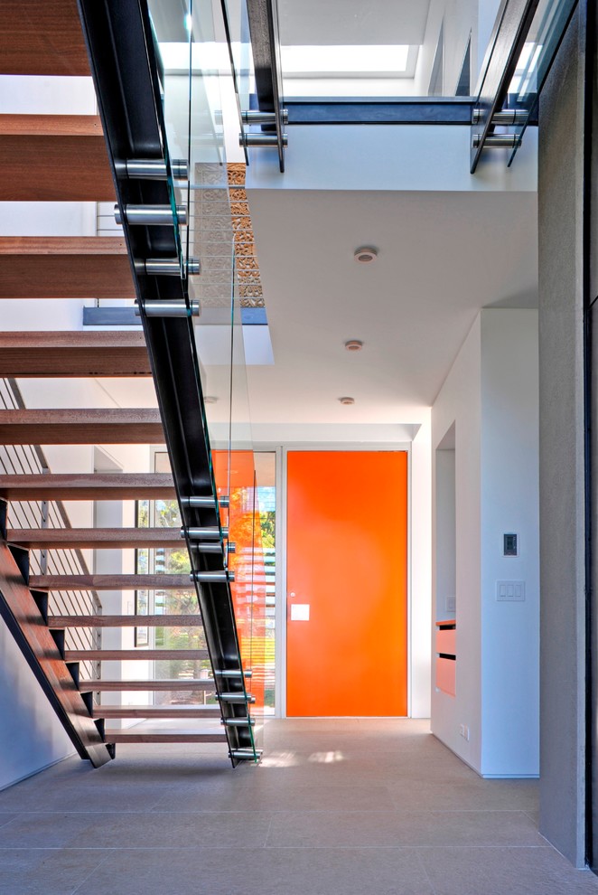 На фото: огромная узкая прихожая в стиле модернизм с белыми стенами, полом из известняка, поворотной входной дверью и оранжевой входной дверью с