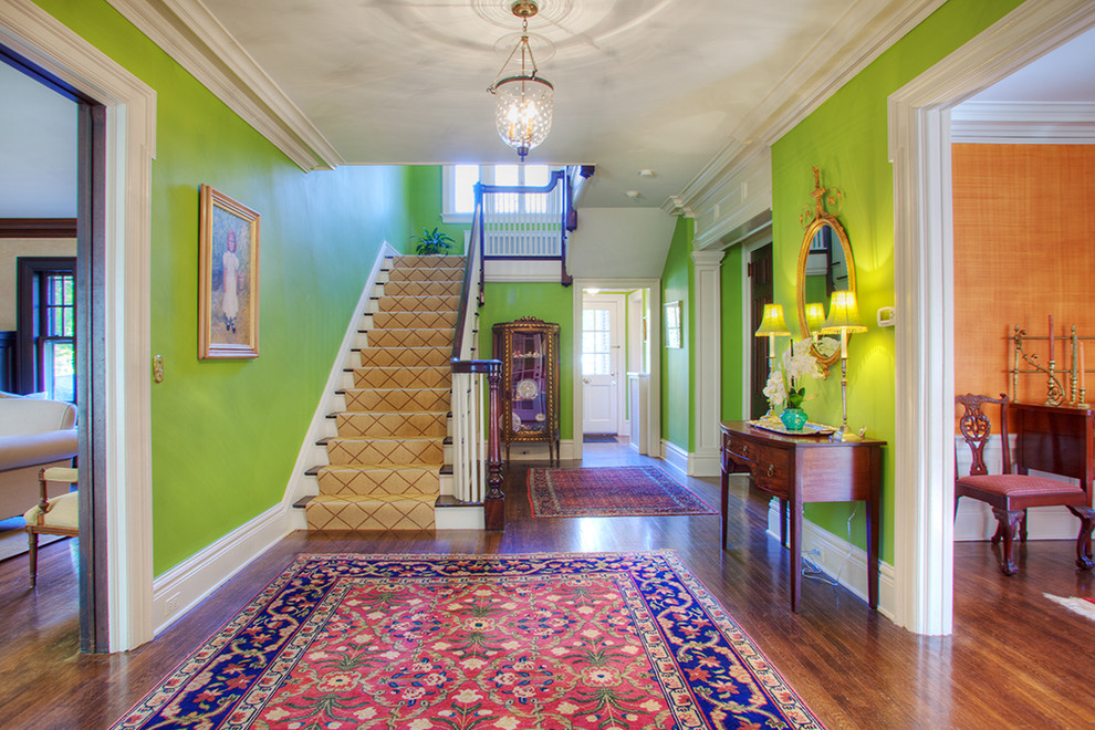 Cette image montre une entrée traditionnelle avec un couloir, un mur vert, parquet foncé et un sol marron.