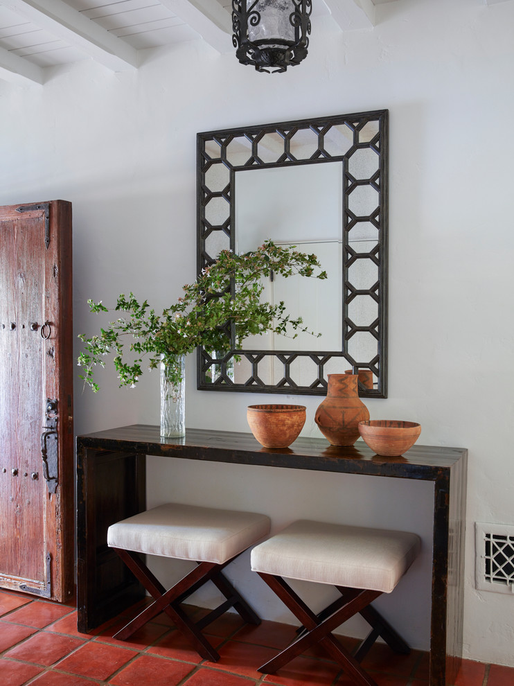 Пример оригинального дизайна: фойе в средиземноморском стиле с белыми стенами, полом из терракотовой плитки, одностворчатой входной дверью, входной дверью из дерева среднего тона и красным полом