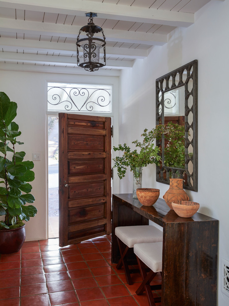 На фото: фойе в средиземноморском стиле с белыми стенами, полом из терракотовой плитки, одностворчатой входной дверью, входной дверью из дерева среднего тона и красным полом с
