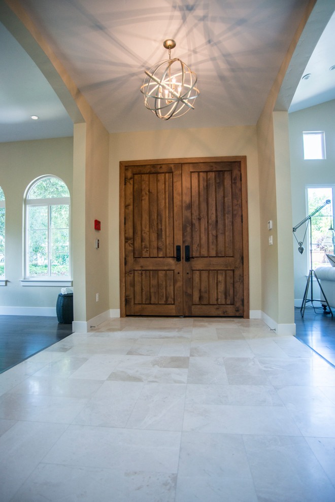 Cette image montre un hall d'entrée traditionnel de taille moyenne avec un mur beige, un sol en marbre, une porte double, une porte en bois foncé et un sol beige.