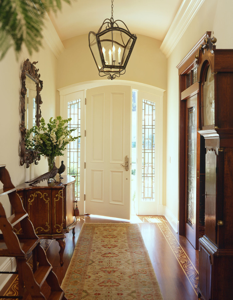 Idee per un corridoio classico con pareti beige, pavimento in legno massello medio, una porta singola e una porta bianca