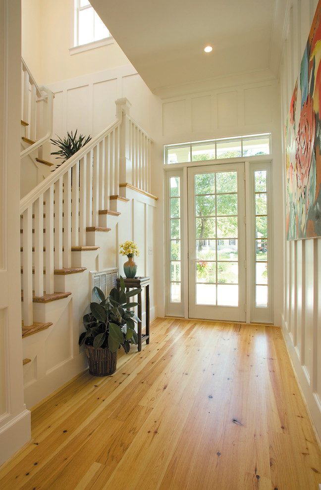 Réalisation d'un grand hall d'entrée champêtre avec un mur blanc, un sol en bois brun, une porte simple et une porte blanche.