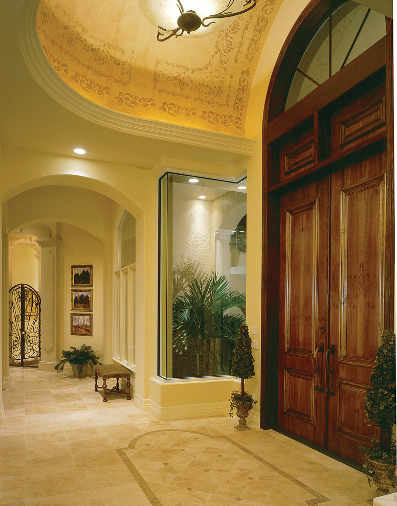 Cette image montre un grand hall d'entrée méditerranéen avec un mur beige, un sol en travertin, une porte double et une porte en bois foncé.