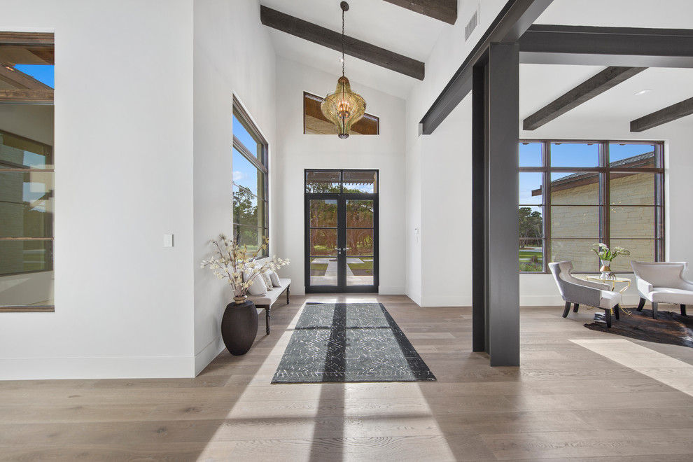 オースティンにあるラグジュアリーな広いトランジショナルスタイルのおしゃれな玄関ロビー (白い壁、磁器タイルの床、金属製ドア、茶色い床) の写真