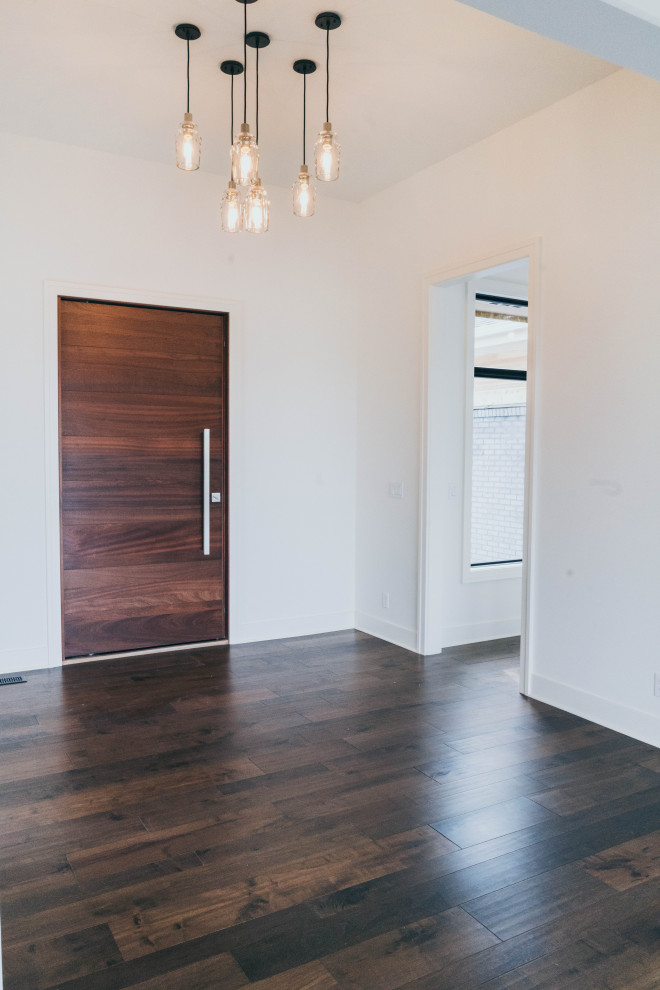 Cette photo montre une grande porte d'entrée moderne avec un mur blanc, parquet foncé, une porte pivot, une porte en bois brun et un sol marron.