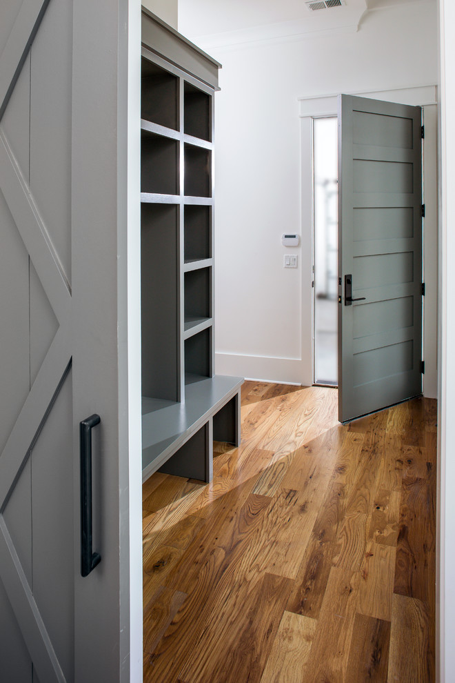 Réalisation d'une entrée minimaliste de taille moyenne avec un vestiaire, un mur blanc, un sol en bois brun, une porte simple et une porte grise.