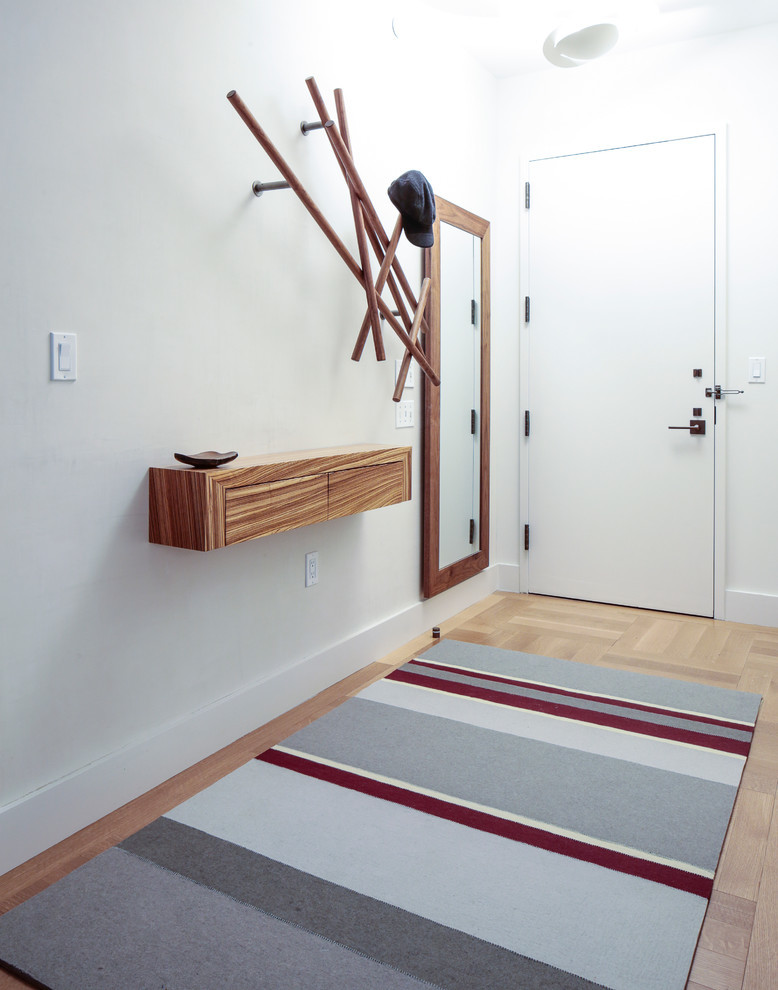 Example of a small minimalist light wood floor entryway design in New York with white walls and a white front door