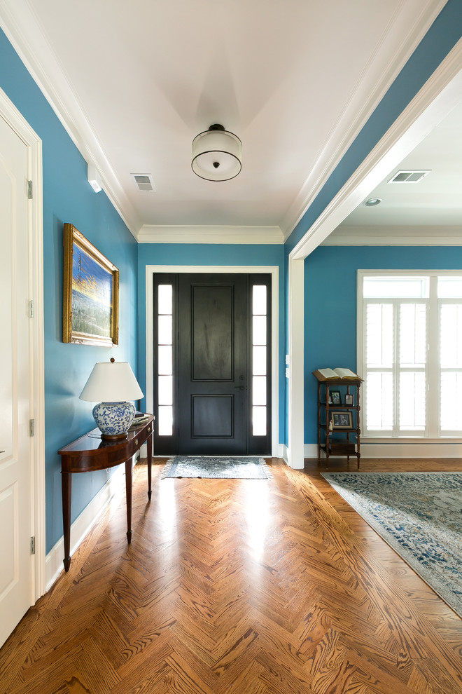 Cette image montre un hall d'entrée traditionnel avec un mur bleu, un sol en bois brun, une porte simple et une porte noire.