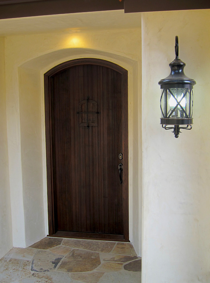 Cette image montre une porte d'entrée méditerranéenne de taille moyenne avec un mur blanc, un sol en calcaire, une porte simple, une porte en bois foncé et un sol multicolore.