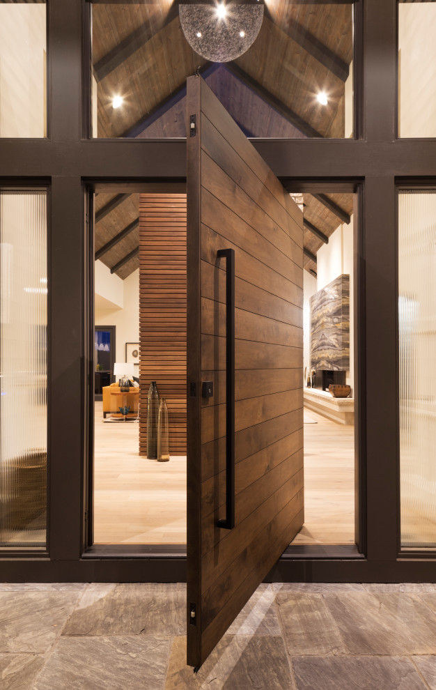 Aménagement d'une très grande porte d'entrée moderne avec parquet clair, une porte pivot, une porte en bois foncé et un sol marron.