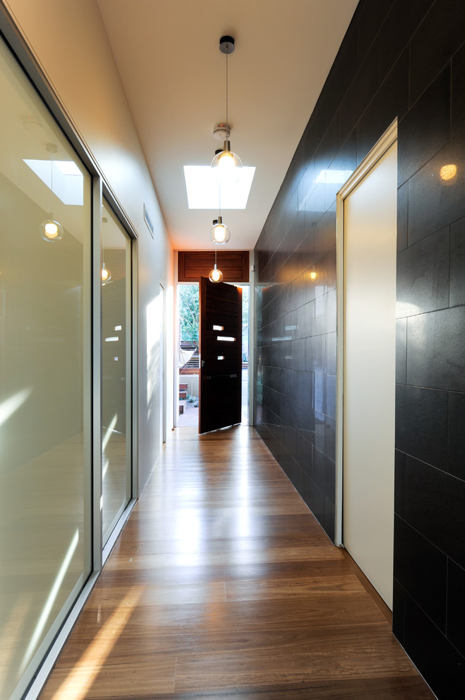 Idées déco pour une porte d'entrée contemporaine avec un sol en bois brun, une porte pivot et une porte en bois brun.