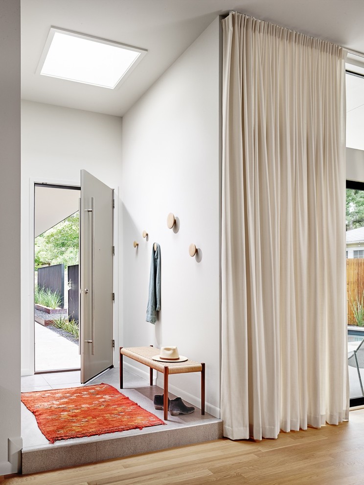 Cette image montre un vestibule design avec un mur blanc, parquet clair, une porte simple et une porte grise.