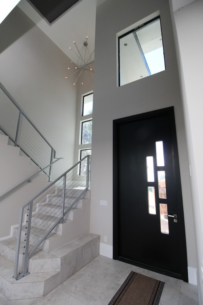 Réalisation d'une grande porte d'entrée design avec un mur gris, une porte simple et une porte noire.