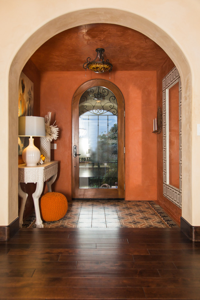 Cette image montre une entrée méditerranéenne de taille moyenne avec un couloir, un mur orange, parquet foncé, une porte simple, une porte en verre et un sol marron.