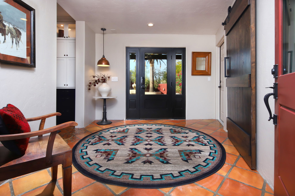 フェニックスにあるサンタフェスタイルのおしゃれな玄関ドア (白い壁、テラコッタタイルの床、黒いドア、赤い床) の写真
