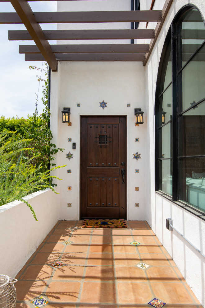 На фото: входная дверь среднего размера в средиземноморском стиле с белыми стенами, полом из терракотовой плитки, одностворчатой входной дверью и входной дверью из темного дерева