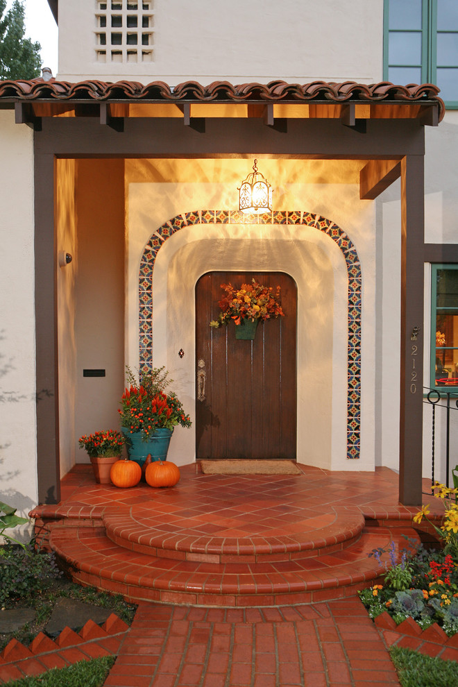 На фото: входная дверь среднего размера в средиземноморском стиле с одностворчатой входной дверью, белыми стенами и входной дверью из темного дерева