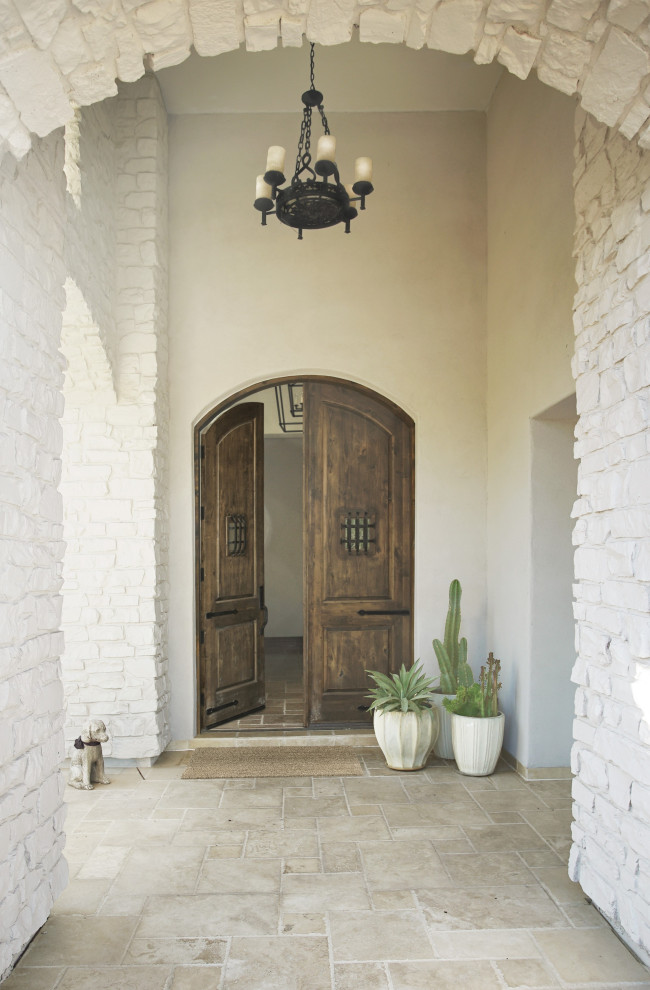 Modelo de puerta principal mediterránea grande con paredes blancas, suelo de piedra caliza, puerta doble, puerta de madera oscura, suelo beige, madera y ladrillo