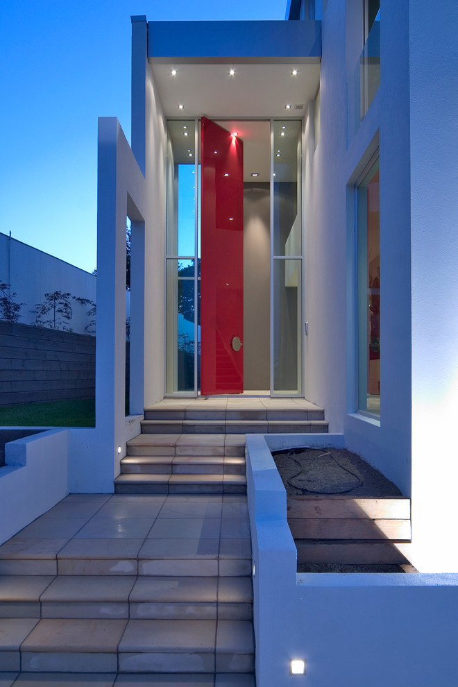 Modern inredning av en stor entré, med en pivotdörr och en röd dörr