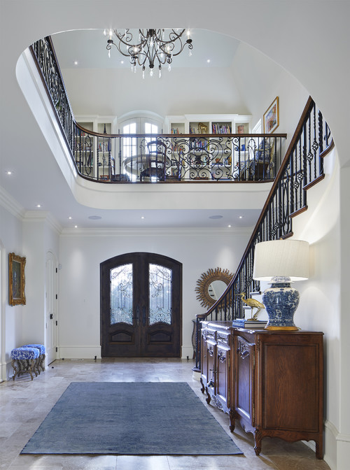 elegant grand entryway with curved staircase, chandelier, dark furniture and blue rug