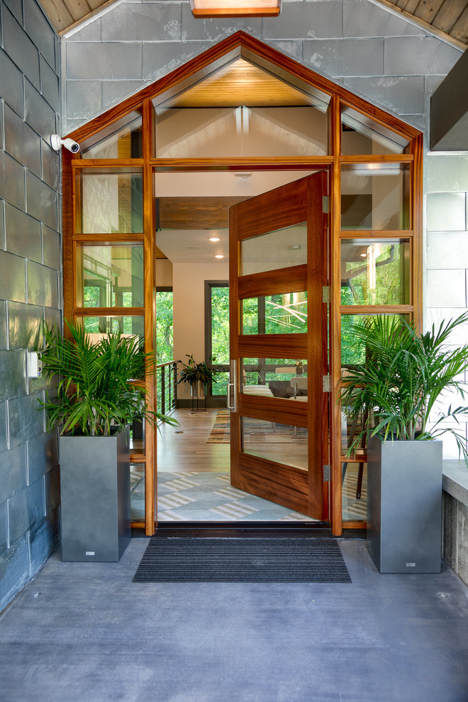 На фото: входная дверь среднего размера в стиле модернизм с серебряными стенами, бетонным полом, одностворчатой входной дверью и входной дверью из дерева среднего тона