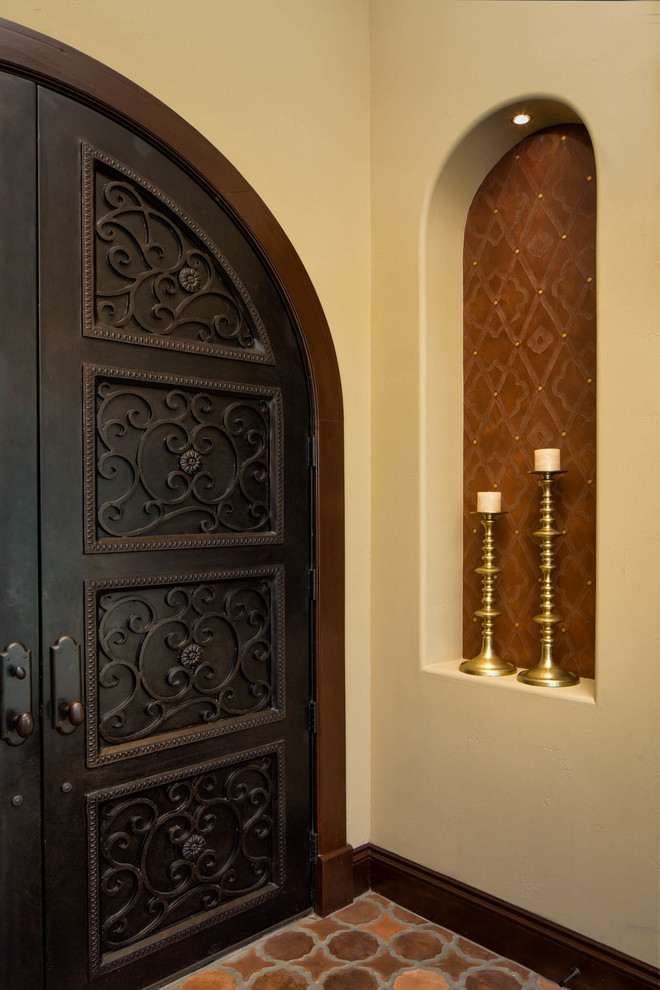 Aménagement d'une entrée classique avec tomettes au sol, une porte double et une porte métallisée.