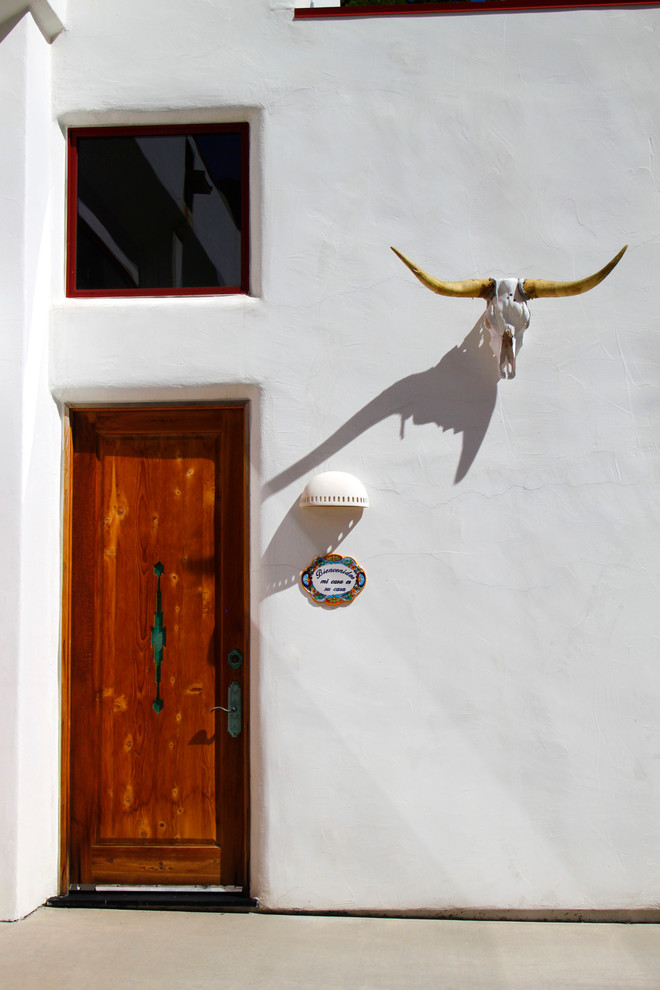 アルバカーキにある中くらいなサンタフェスタイルのおしゃれな玄関ドア (白い壁、木目調のドア、コンクリートの床) の写真