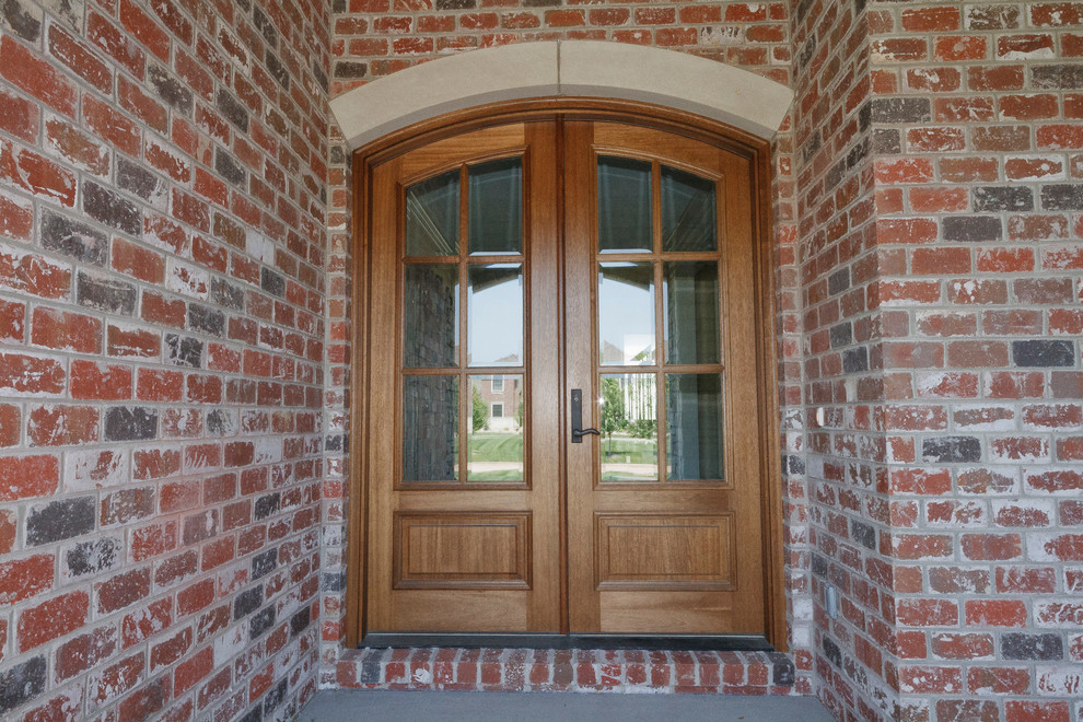 Réalisation d'une grande porte d'entrée tradition avec une porte double, une porte en bois brun et un mur rouge.