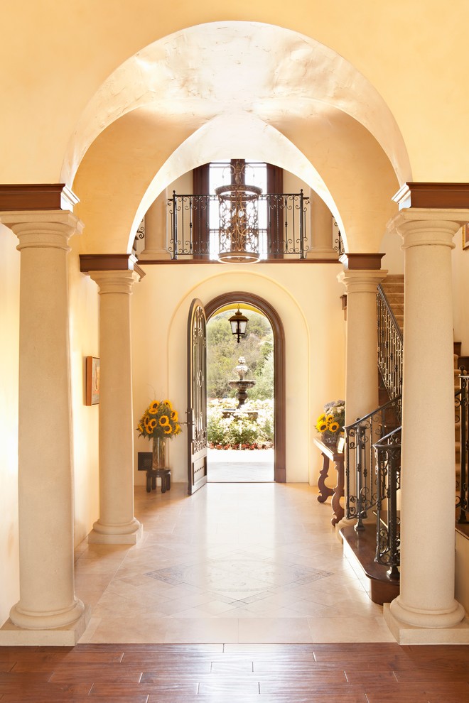 На фото: фойе в средиземноморском стиле с бежевыми стенами, одностворчатой входной дверью, входной дверью из темного дерева и бежевым полом