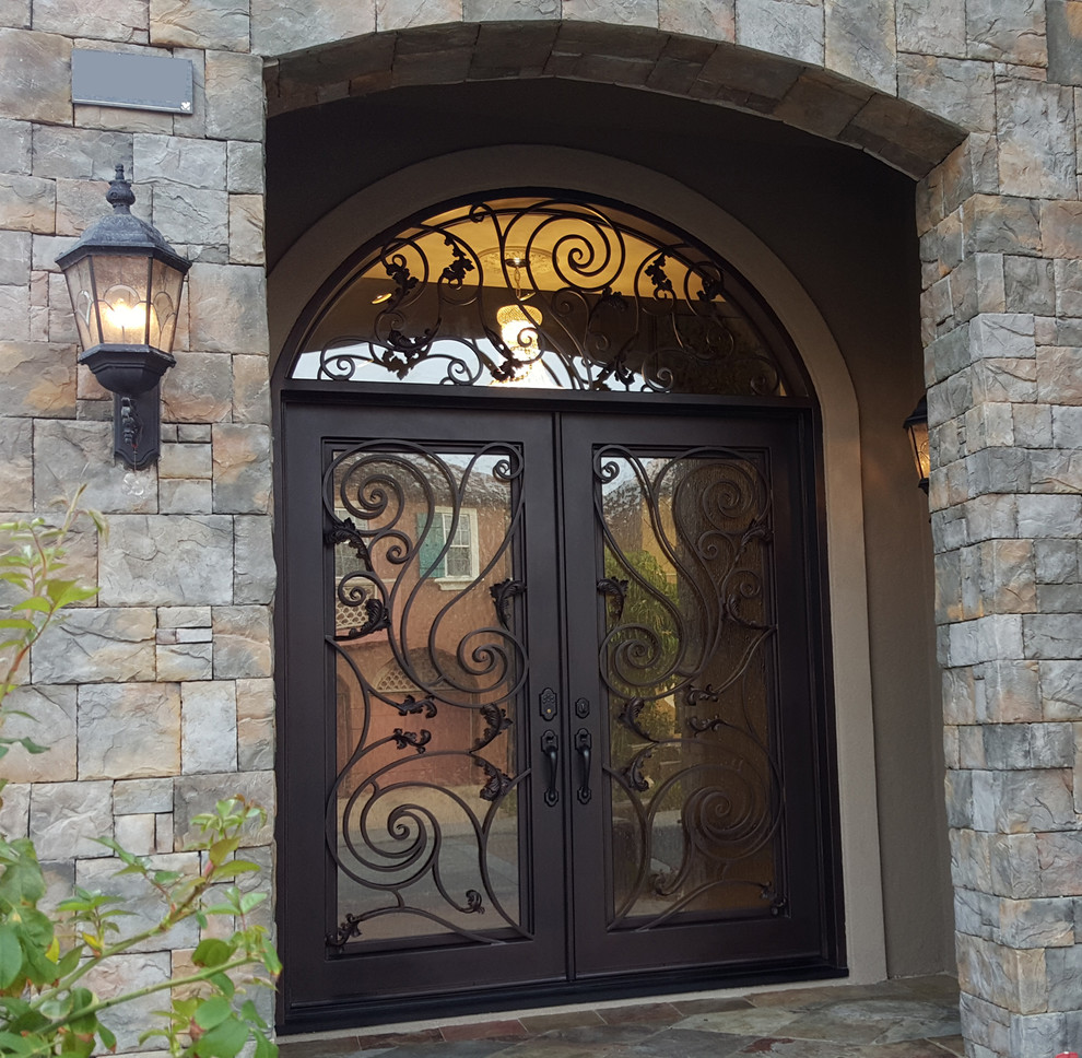 На фото: большая входная дверь в средиземноморском стиле с коричневыми стенами, полом из сланца, двустворчатой входной дверью, коричневой входной дверью и бежевым полом с