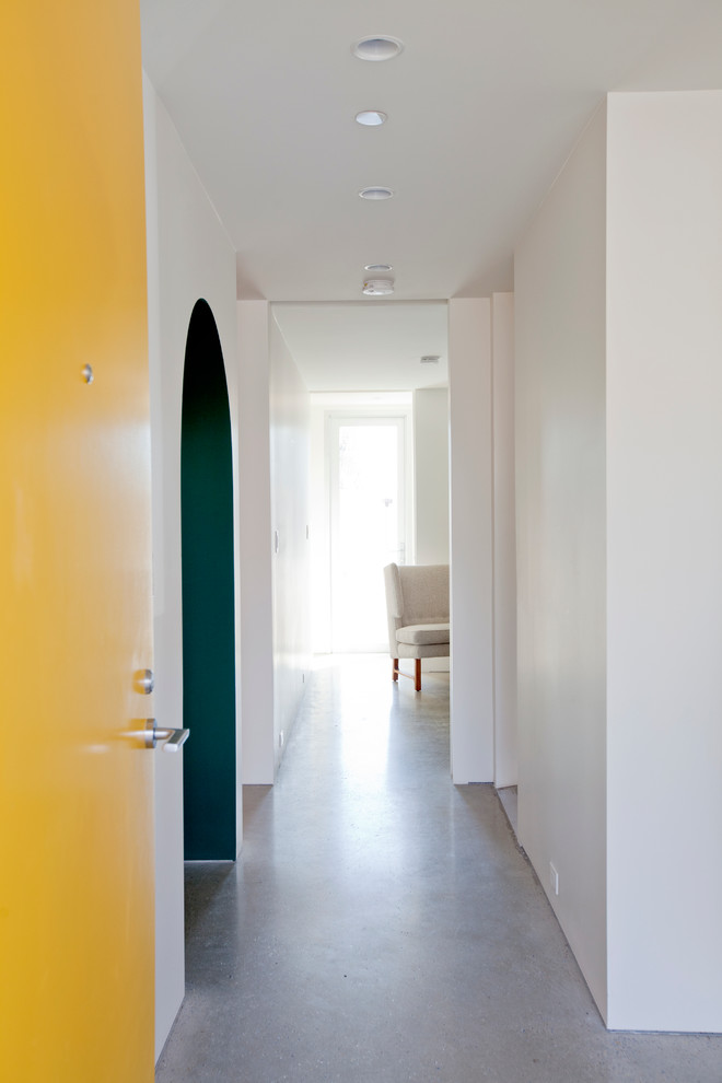 Réalisation d'une entrée design avec sol en béton ciré, une porte simple et une porte jaune.