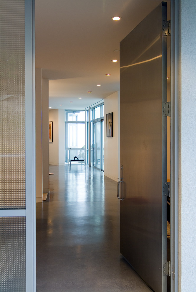 Cette image montre une entrée minimaliste de taille moyenne avec un mur blanc, sol en béton ciré, une porte simple et une porte métallisée.