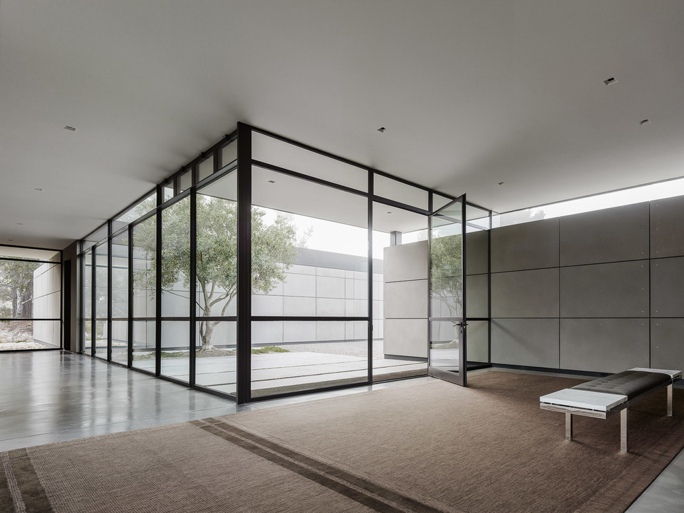 На фото: огромный вестибюль в современном стиле с серыми стенами, бетонным полом, поворотной входной дверью, стеклянной входной дверью и серым полом с
