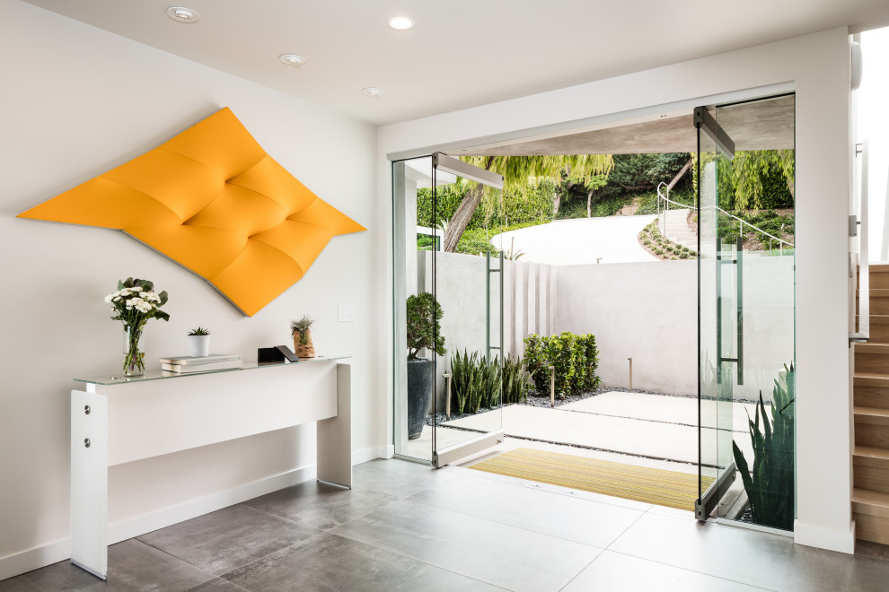 Photo of a large contemporary front door in Orange County with white walls, porcelain flooring, a pivot front door, a glass front door and grey floors.