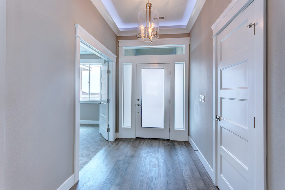 Aménagement d'une petite entrée classique avec un couloir, un mur gris, un sol en bois brun, une porte simple, une porte blanche et un sol gris.
